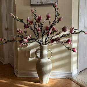 May include: A white ceramic vase with two handles, filled with a large arrangement of pink and white magnolia blossoms.