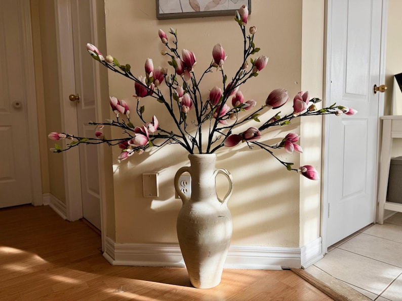 May include: A white ceramic vase with two handles, filled with a bouquet of pink and white magnolia flowers.