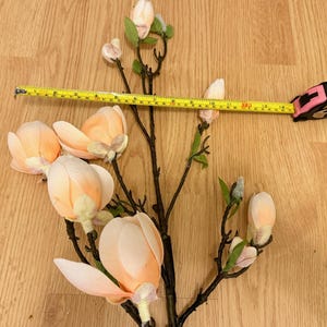 May include: A branch of artificial magnolia flowers with pink and white blossoms. The branch is measured with a tape measure, showing it is 17 inches long.