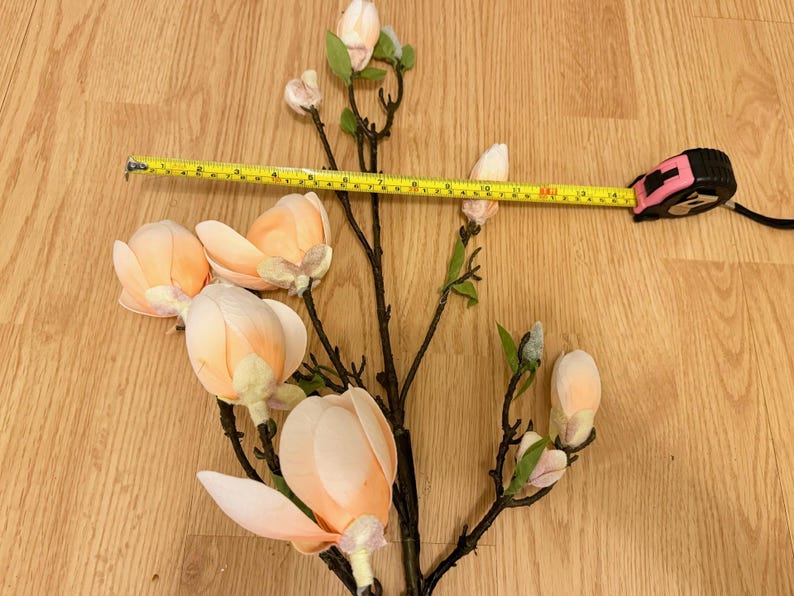 May include: A branch of artificial magnolia flowers with pink and white blossoms. The branch is measured with a tape measure, showing it is 17 inches long.