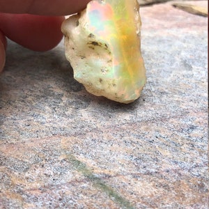 Puede incluir: Una piedra preciosa de &oacute;palo en bruto, blanca, con destellos iridiscentes de amarillo, verde y azul.