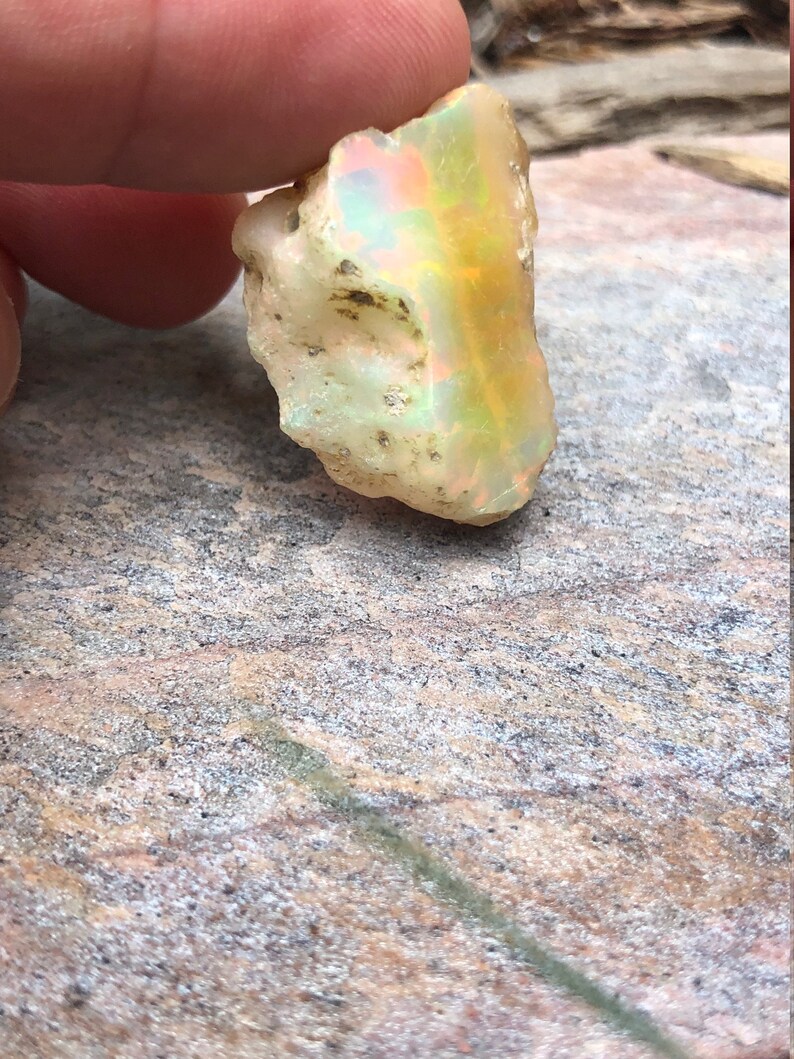 Puede incluir: Una piedra preciosa de &oacute;palo en bruto, blanca, con destellos iridiscentes de amarillo, verde y azul.