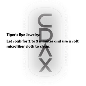 May include: A white rectangular graphic with rounded corners featuring the vertical black text CDAX. The text reads: Tiger's Eye Jewelry: Let soak for 2 to 3 minutes and use a soft microfiber cloth to clean. The background contains faint repeating text.