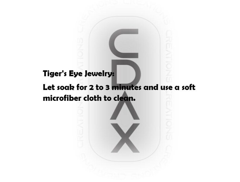 May include: A white rectangular graphic with rounded corners featuring the vertical black text CDAX. The text reads: Tiger's Eye Jewelry: Let soak for 2 to 3 minutes and use a soft microfiber cloth to clean. The background contains faint repeating text.