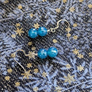 May include: A pair of dangle earrings featuring two faceted, round, bright blue beads on each piece. The beads are connected by silver-toned wire and attached to silver-toned ear hooks, creating a simple and elegant design for everyday wear.