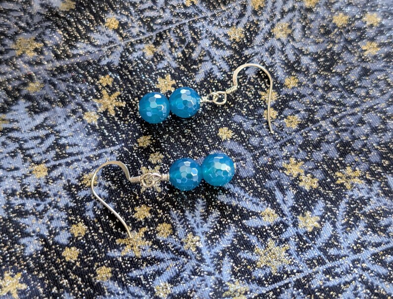May include: A pair of dangle earrings featuring two faceted, round, bright blue beads on each piece. The beads are connected by silver-toned wire and attached to silver-toned ear hooks, creating a simple and elegant design for everyday wear.
