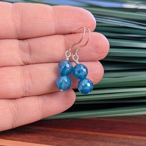May include: A pair of dangle earrings featuring two faceted, round, bright blue beads stacked vertically on each earring. The beads are connected by silver-toned wire and attached to silver-toned ear hooks, creating a simple drop design.