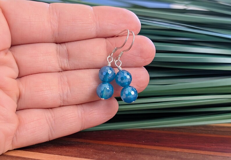 May include: A pair of dangle earrings featuring two faceted, round, bright blue beads stacked vertically on each earring. The beads are connected by silver-toned wire and attached to silver-toned ear hooks, creating a simple drop design.