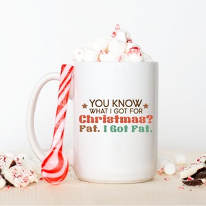 May include: A white ceramic mug filled with marshmallows and a red and white striped candy spoon. The mug has the text "YOU KNOW WHAT I GOT FOR Christmas? Fat. I Got Fat." in brown, red, and green.