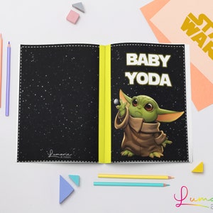 Puede incluir: Un libro para colorear en blanco y negro con una encuadernación amarilla. La portada presenta una imagen de dibujos animados de Baby Yoda de Star Wars. El título "Baby Yoda" está impreso en letras blancas sobre un fondo negro. La contraportada es negra con un patrón estrellado y el texto "Lumarie all creations" impreso en blanco.