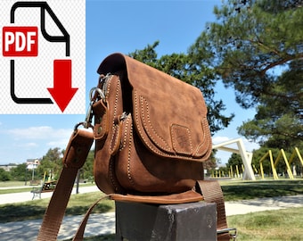 May include: A brown leather shoulder bag with a zippered pocket and a flap closure. The bag has a long adjustable strap and is sitting on a wooden surface.