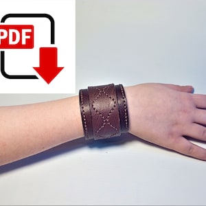 Puede incluir: Un brazalete de cuero marrón con un patrón de costura en forma de diamante. El brazalete se lleva en la muñeca.