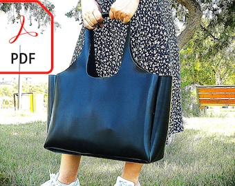 May include: A large, dark blue tote bag with a rectangular shape and integrated handles. The bag is held by a person in a floral dress, with a park setting in the background. A PDF icon is visible in the upper left corner.