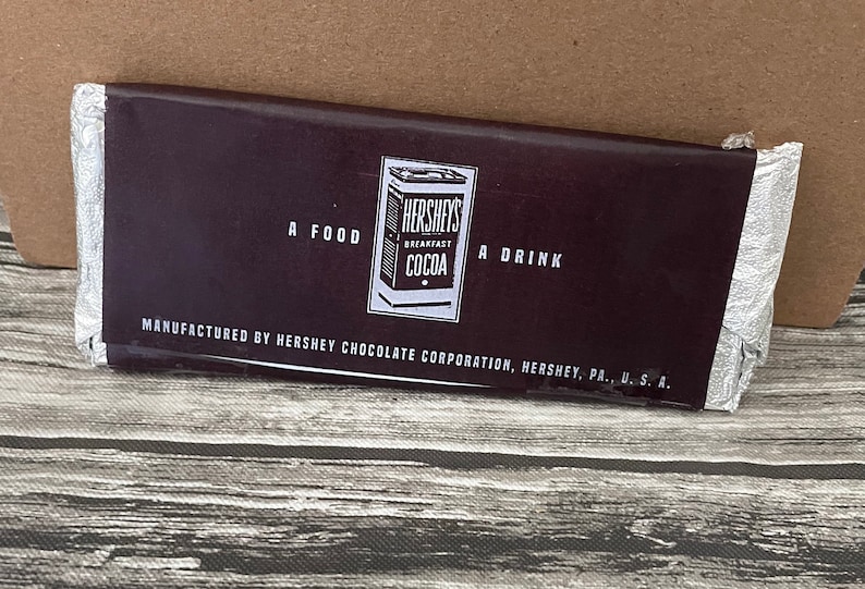 Puede incluir: Envase de cacao Hershey's Breakfast. El envoltorio marr&oacute;n oscuro presenta el logotipo de Hershey's y el texto "A Food, A Drink". El embalaje de papel de aluminio plateado es parcialmente visible. Tambi&eacute;n es visible el texto "Manufactured by Hershey Chocolate Corporation, Hershey, PA., U.S.A.".