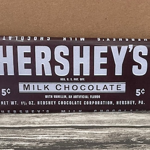 以下が含まれることがあります： 茶色の包装と銀色のホイルが付いたハーシーのミルクチョコレートバー。 包装には、ハーシーのロゴが白で表示され、ミルクチョコレート、42.5g、5セントであることを示すテキストが記載されています。