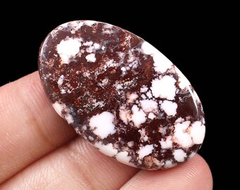 May include: Oval shaped cabochon gemstone with a brown and white marbled pattern. The stone has a speckled appearance with white spots on a brown background.
