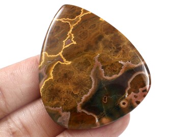 May include: A brown, green, and pink agate cabochon with a unique, intricate pattern. The stone is polished and has a smooth, glossy finish.