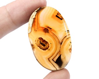 May include: A smooth, oval-shaped agate gemstone with a brown, white, and orange banded pattern. The agate has a translucent appearance and shows intricate details of the banding.