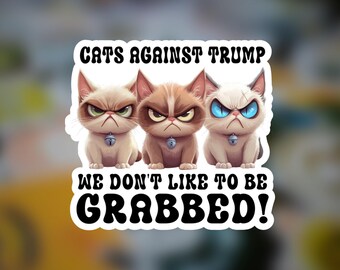 Könnte beinhalten: Ein rechteckiger Aufkleber mit drei mürrisch aussehenden Katzen mit Halsbändern und Glöckchen. Der Text lautet oben CATS AGAINST TRUMP und unten WE DON'T LIKE TO BE GRABBED! in fetter schwarzer Schrift auf einem weißen Hintergrund.