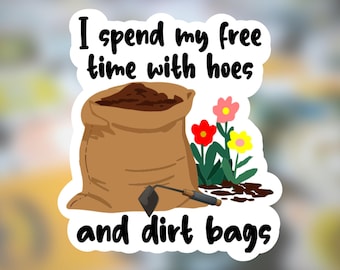 Könnte beinhalten: Ein weißer Aufkleber mit dem Text "I spend my free time with hoes and dirt bags." Der Aufkleber zeigt einen braunen Jutesack mit Erde, ein kleines Gartengerät und bunte Blumen.
