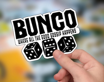 Könnte beinhalten: Ein weißer Aufkleber mit schwarzem Text, der "BUNCO WHERE ALL THE GOOD GOSSIP HAPPENS" lautet. Unter dem Text sind drei schwarze Würfel mit weißen Punkten abgebildet.