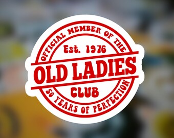 Könnte beinhalten: Ein weißer Aufkleber mit einem roten kreisförmigen Design. Der Text lautet "OFFICIAL MEMBER OF THE OLD LADIES CLUB" mit "Est. 1976" in der Mitte und "50 YEARS OF PERFECTION" unten. Der Aufkleber hat einen Vintage-Look.