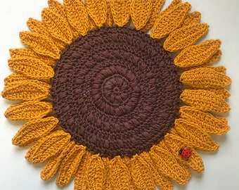 May include: A handmade crochet sunflower with a brown center and yellow petals. A small red ladybug is on one of the petals. The sunflower is a decorative item, likely a coaster or trivet.