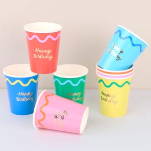 May include: A collection of six colorful paper cups featuring a wavy line pattern near the rim and the text Happy Birthday in gold foil lettering. The cups are red, blue, green, light blue, pink, and yellow, each with a contrasting wavy line.