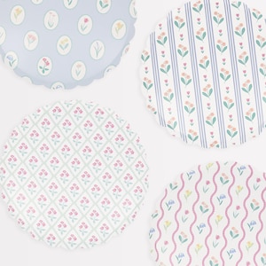 May include: Four round paper plates with scalloped edges feature different floral patterns. The plates are white with pastel pink, blue, and yellow flowers.