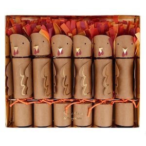 May include: A set of six brown paper turkey-shaped party crackers arranged in a gold box. Each turkey features a kraft paper body, gold foil beak, red wattle, and a fringe of orange, red, and purple tissue paper at the top. Text reads Meri Meri 6 Crackers.