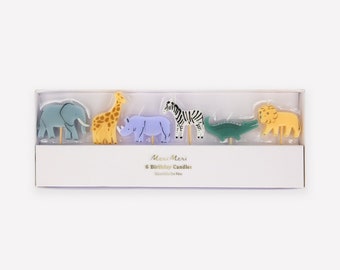 May include: A box of six Meri Meri birthday candles featuring animal designs. The candles are in the shape of an elephant, giraffe, rhinoceros, zebra, crocodile, and lion. The box is white with gold lettering.