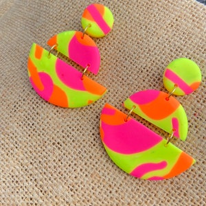 May include: A pair of neon green, pink, and orange statement earrings with a geometric design. The earrings are made of polymer clay and have a gold-tone metal finding.