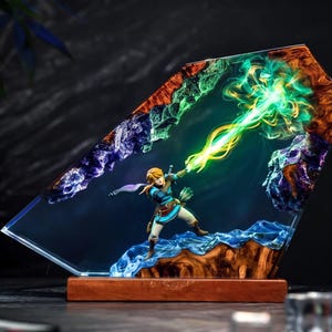 May include: A decorative resin and wood lamp featuring a miniature figure of a blonde warrior in blue tunic and brown boots, casting a bright green light beam. The piece is set in a jagged, translucent blue and purple resin frame.