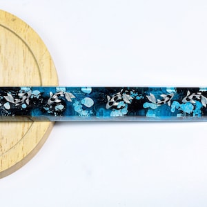 May include: A rectangular resin object with a koi fish design. The design features black and white koi fish swimming in a blue and black water-like background. The object is set on a wooden surface.