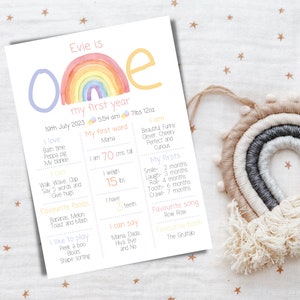 May include: A colorful printable chart celebrating a baby's first year. The chart features a rainbow, the number one, and details about the baby's milestones, including weight, height, first words, favorite foods, and songs. The chart is decorated with a watercolor rainbow and stars.