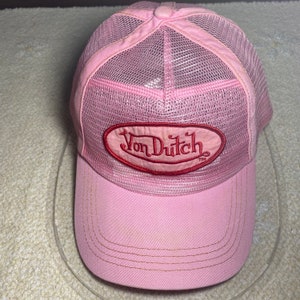 Könnte beinhalten: Rosafarbene Trucker-Cap mit Mesh-Rückseite und gebogenem Schirm. Auf der Vorderseite befindet sich ein rotes ovales Patch mit dem Text "Von Dutch". Die Cap hat einen Knopf oben.
