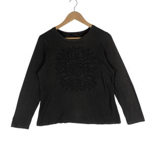 May include: Dark gray long-sleeve shirt with a crew neck. The shirt features a black floral mandala design on the front. The shirt is hanging on a wooden hanger against a white background.
