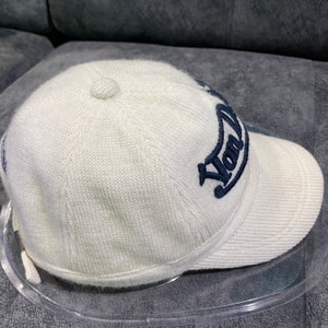 K&ouml;nnte beinhalten: Cremefarbene Baseballkappe mit gebogenem Schirm. Auf der Kappe ist das Wort "York" in marineblauer Schrift gestickt. Die Kappe besteht aus einem strukturierten Strickmaterial und hat einen kleinen Knopf oben.