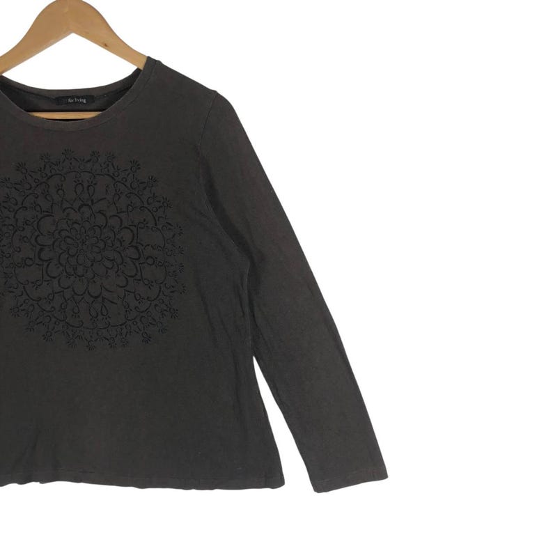 May include: A dark brown long-sleeve shirt with a crew neck. The shirt features a detailed, symmetrical floral design on the front. The shirt is made of a soft material and is suitable for casual wear.