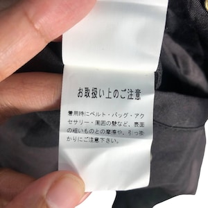 May include: A white tag with Japanese text, held by a hand, attached to a black garment. The text provides care instructions, warning against friction and snagging during wear.