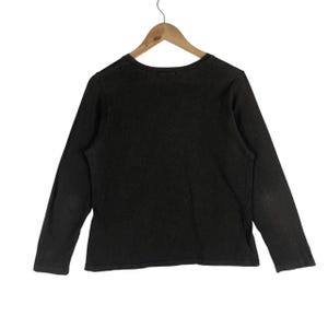 May include: A dark brown long-sleeve shirt hanging on a wooden hanger. The shirt has a crew neck and a slightly faded appearance. The sleeves are long and the fabric appears to be a soft material.