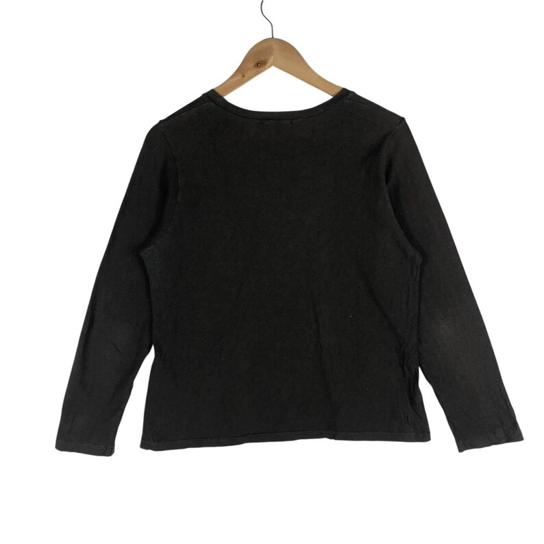May include: A dark brown long-sleeve shirt hanging on a wooden hanger. The shirt has a crew neck and a slightly faded appearance. The sleeves are long and the fabric appears to be a soft material.