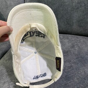 K&ouml;nnte beinhalten: Cremefarbene Baseballkappe mit gebogenem Schirm. Die Innenseite hat dunkelblaue gestickte Schrift und ein Markenetikett. Die Kappe ist aus einem strukturierten Stoff gefertigt.