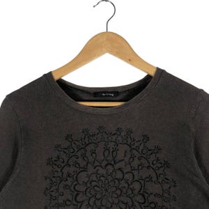 May include: A dark gray long-sleeve shirt with a black floral mandala design on the front. The shirt has a crew neck and the text "for living" is printed on the collar.