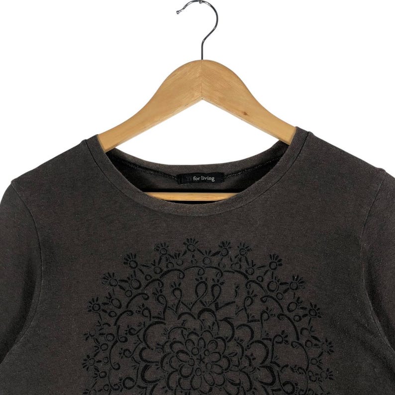 May include: A dark gray long-sleeve shirt with a black floral mandala design on the front. The shirt has a crew neck and the text "for living" is printed on the collar.