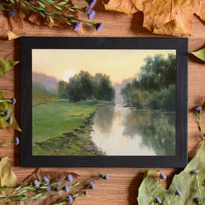 Pode incluir: Uma pintura de paisagem emoldurada retratando um rio que flui atrav&eacute;s de um prado verde ao nascer do sol. A cena apresenta &aacute;rvores verdes exuberantes, um c&eacute;u amarelo suave e reflexos na superf&iacute;cie da &aacute;gua, dentro de uma moldura preta.