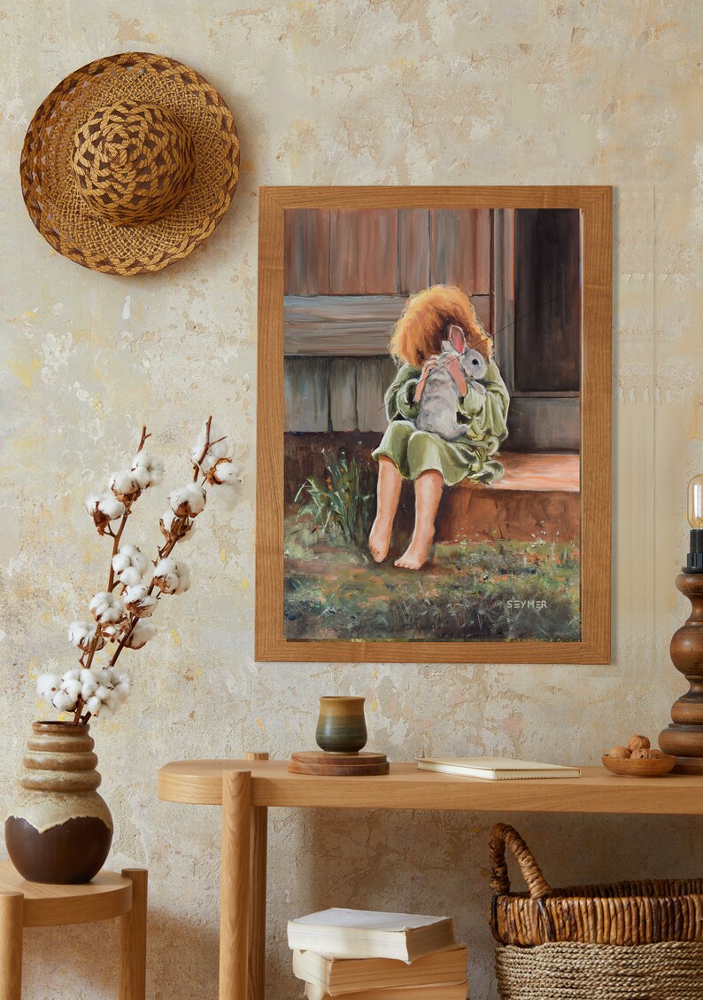 May include: A framed painting of a young girl in a green dress holding a white rabbit. The painting is set in a rustic outdoor setting with a wooden door and green grass.