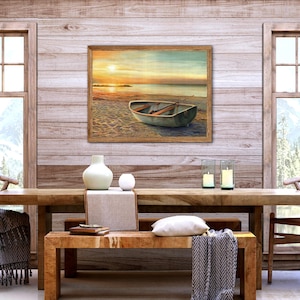 Op de afbeelding: Een rechthoekige ingelijste kunstdruk met een kleine roeiboot op een zandstrand bij zonsondergang, met zacht gouden licht dat reflecteert op het water en de horizon, in een kamer met een houten tafel, stoelen en kaarsen.