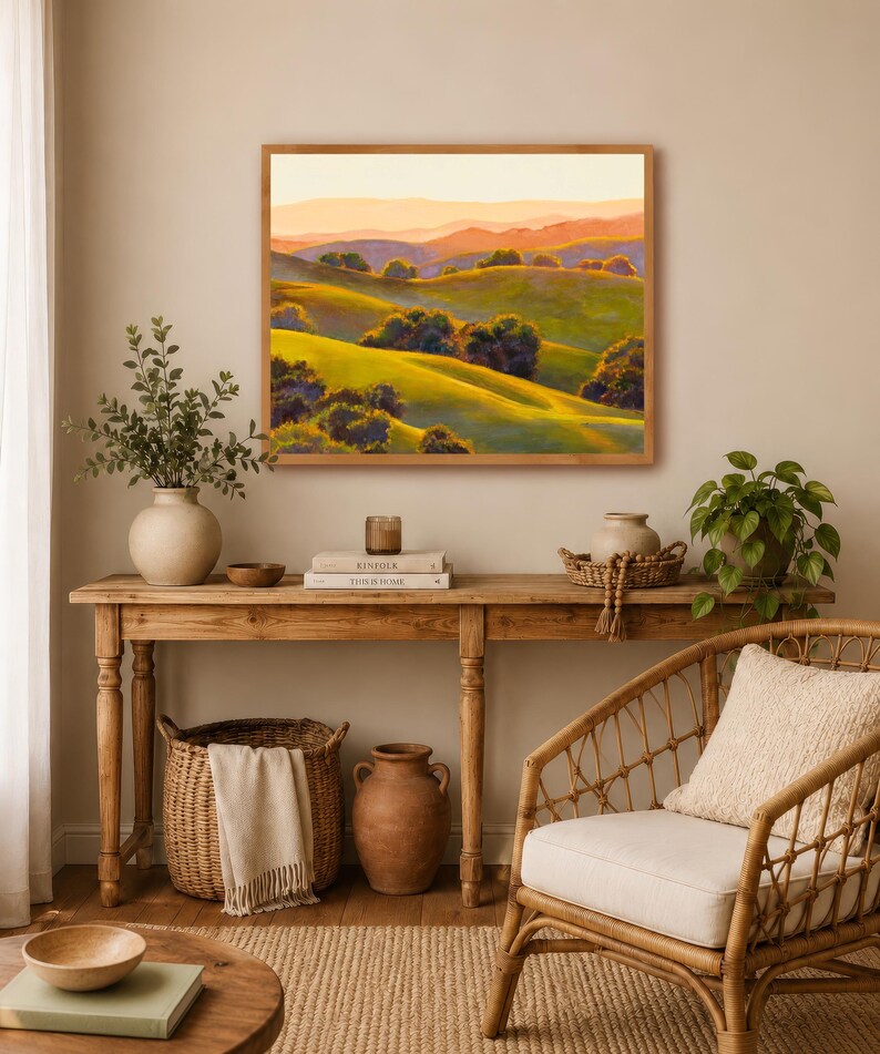 Peut inclure: Une peinture de paysage rectangulaire dans un cadre en bois clair repr&eacute;sentant des collines verdoyantes, des arbres vert fonc&eacute; et des montagnes lointaines aux teintes orang&eacute;es sous un ciel doux. L'&oelig;uvre est expos&eacute;e au-dessus d'une console.