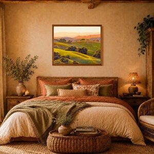 Peut inclure: Une peinture de paysage rectangulaire dans un cadre en bois brun repr&eacute;sentant des collines verdoyantes avec des arbres &eacute;pars sous un ciel de coucher de soleil chaud. L'&oelig;uvre est expos&eacute;e sur un mur beige au-dessus d'un lit aux tons rouille et olive.